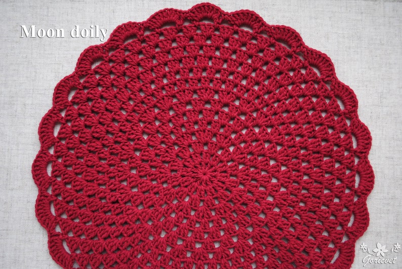 Pu&ograve; includere: Un centrino all'uncinetto rosso con un design circolare. Il centrino &egrave; realizzato con un filo sottile e ha un aspetto delicato e traforato. Il testo "Moon doily" &egrave; visibile nell'angolo in alto a sinistra dell'immagine.
