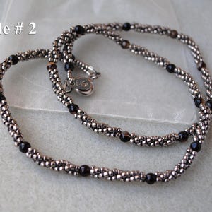 Op de afbeelding: Een zilveren en zwarte kralenketting met een zilveren sluiting. De ketting is gemaakt van kleine, ronde kralen en is in een dubbele streng gelegd.