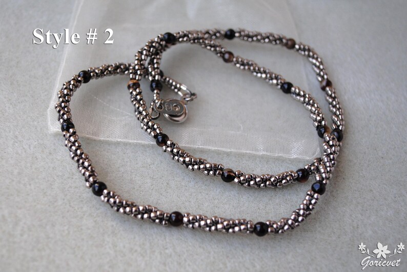 Op de afbeelding: Een zilveren en zwarte kralenketting met een zilveren sluiting. De ketting is gemaakt van kleine, ronde kralen en is in een dubbele streng gelegd.