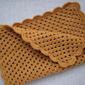 May include: A crocheted baby blanket in a mustard yellow color with a scalloped edge.