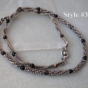 Op de afbeelding: Een zilveren en zwarte kralenketting met een magneetsluiting. De ketting is gelaagd en heeft een subtiele glans. Style #3