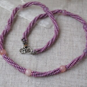 Puede incluir: Un delicado collar de cuentas moradas con un cierre plateado y peque&ntilde;as piedras redondas moradas.