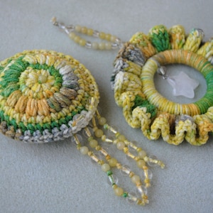 May include: Two crocheted earrings in a green, yellow and white colour scheme. One earring is round with a beaded fringe. The other earring is a flower shape with a white stone in the centre.