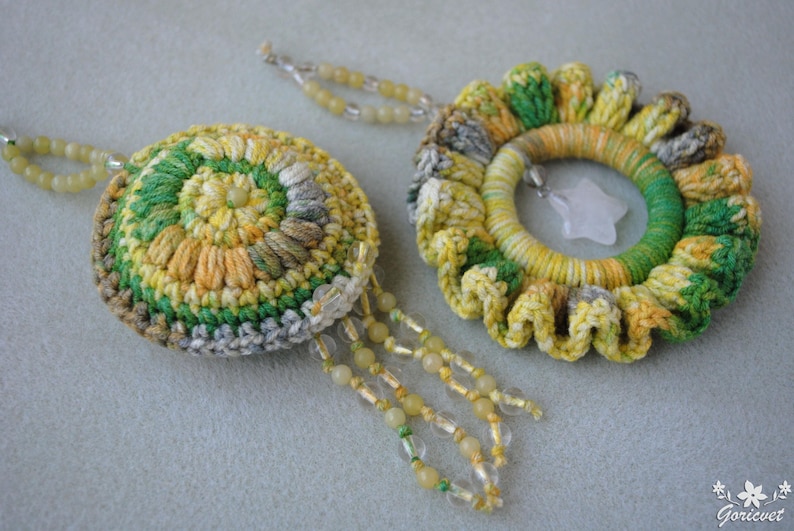 May include: Two crocheted earrings in a green, yellow and white colour scheme. One earring is round with a beaded fringe. The other earring is a flower shape with a white stone in the centre.