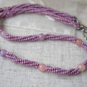 Puede incluir: Un delicado collar de cuentas moradas con un dise&ntilde;o trenzado y detalles de piedras preciosas de color rosa claro.
