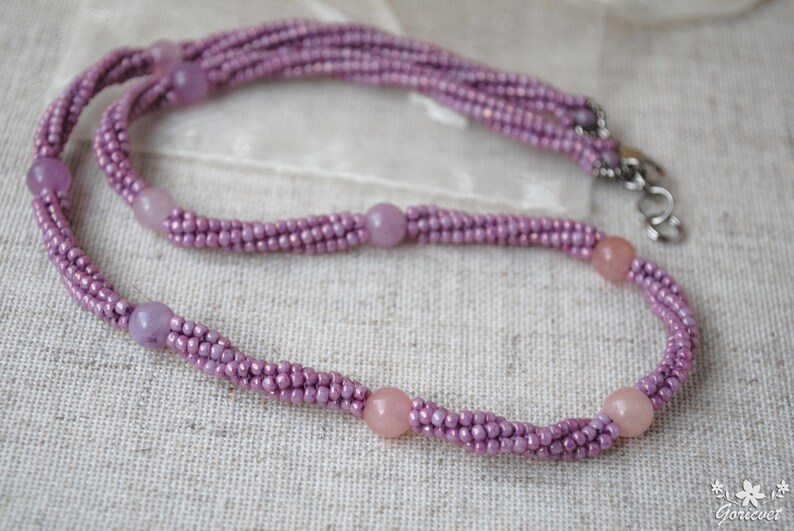 Puede incluir: Un delicado collar de cuentas moradas con un dise&ntilde;o trenzado y detalles de piedras preciosas de color rosa claro.