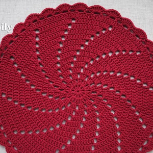 Pu&ograve; includere: Un centrino all'uncinetto rosso con un design a raggiera. Il centrino &egrave; rotondo e ha un bordo smerlato.