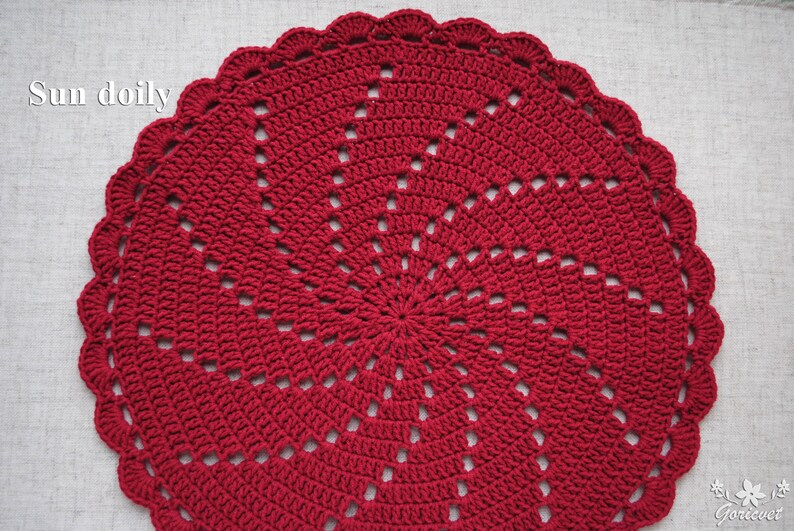 Pu&ograve; includere: Un centrino all'uncinetto rosso con un design a raggiera. Il centrino &egrave; rotondo e ha un bordo smerlato.