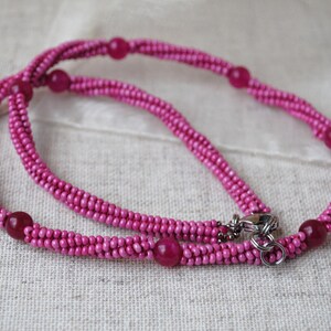 Puede incluir: Un collar de cuentas rosadas con un cierre plateado. El collar est&aacute; hecho de peque&ntilde;as cuentas redondas y tiene un dise&ntilde;o de doble cadena.
