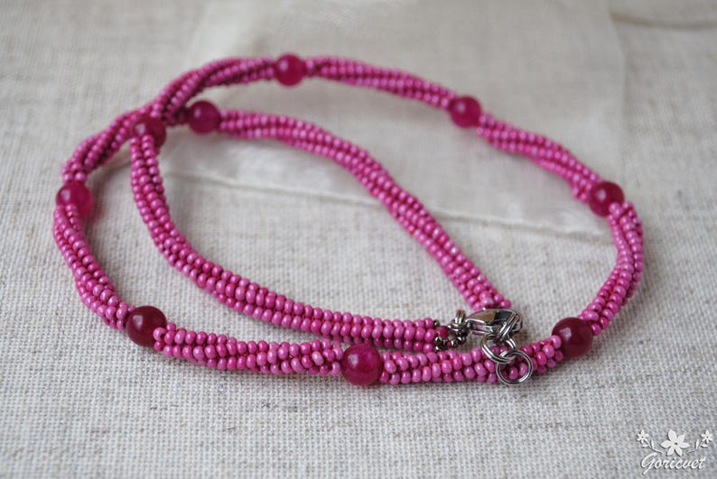 Puede incluir: Un collar de cuentas rosadas con un cierre plateado. El collar est&aacute; hecho de peque&ntilde;as cuentas redondas y tiene un dise&ntilde;o de doble cadena.