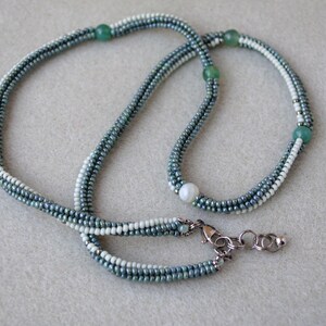 May include: A multi-strand necklace made of small, light blue and white beads. The necklace has a single white pearl bead and three green beads.
