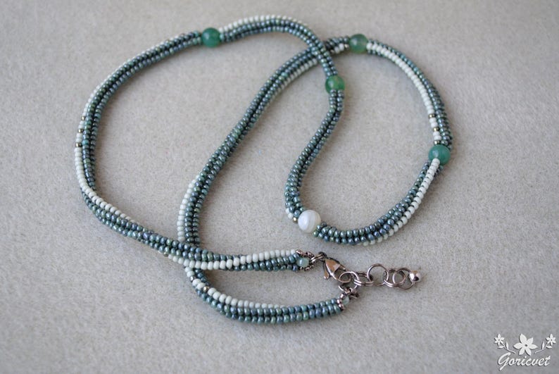 May include: A multi-strand necklace made of small, light blue and white beads. The necklace has a single white pearl bead and three green beads.