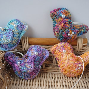 May include: Four crocheted bird ornaments in a wicker basket. The birds are in shades of blue, purple, orange, and green with white pearl accents.