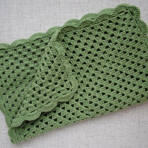 May include: A green crocheted blanket with a scalloped edge. The blanket is folded in half and is lying on a light gray surface.