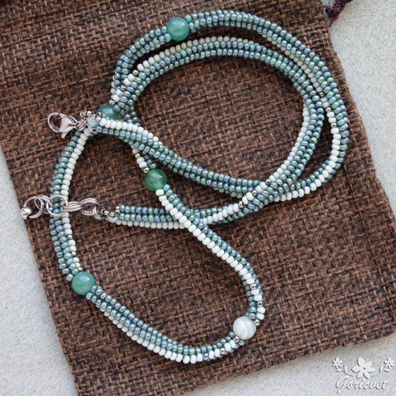 May include: A multi-strand necklace with green and white beads and green gemstone accents. The necklace is made of small beads and has a silver clasp.