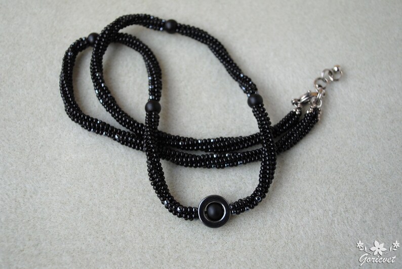 May include: A black beaded necklace with a silver clasp and a black circular pendant.