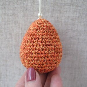 Pu&ograve; includere: Un ornamento a forma di uovo in crochet arancione e giallo. L'uovo &egrave; realizzato con un punto testurizzato e ha una lucentezza sottile.