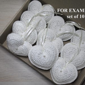 May include: A set of 10 white crocheted heart-shaped ornaments with pearl accents. The hearts are arranged in a box and are ready to be used as decorations. FOR EXAMPLE set of 10