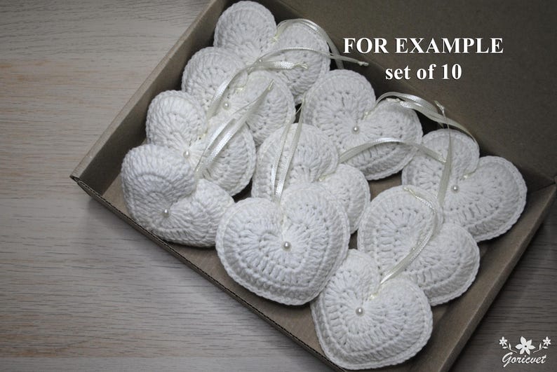 May include: A set of 10 white crocheted heart-shaped ornaments with pearl accents. The hearts are arranged in a box and are ready to be used as decorations. FOR EXAMPLE set of 10