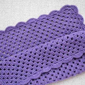 May include: A purple crocheted blanket with a scalloped edge. The blanket is made with a simple stitch pattern and has a soft, textured feel.
