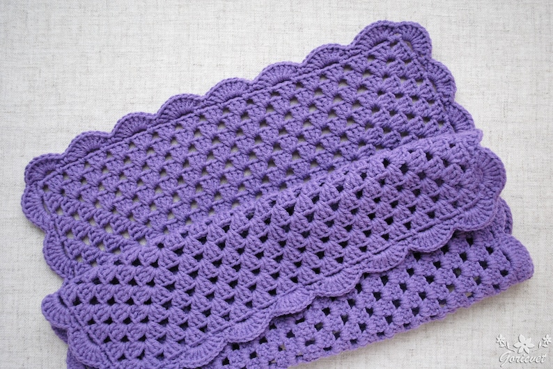 May include: A purple crocheted blanket with a scalloped edge. The blanket is made with a simple stitch pattern and has a soft, textured feel.