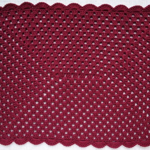 May include: A burgundy crocheted square placemat with a scalloped edge.