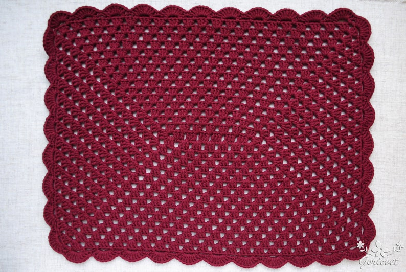 May include: A burgundy crocheted square placemat with a scalloped edge.