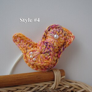 May include: A crocheted bird with a swirl pattern in shades of orange, pink, and purple. The bird has three white pearl beads for eyes. The bird is sitting on a wicker basket.