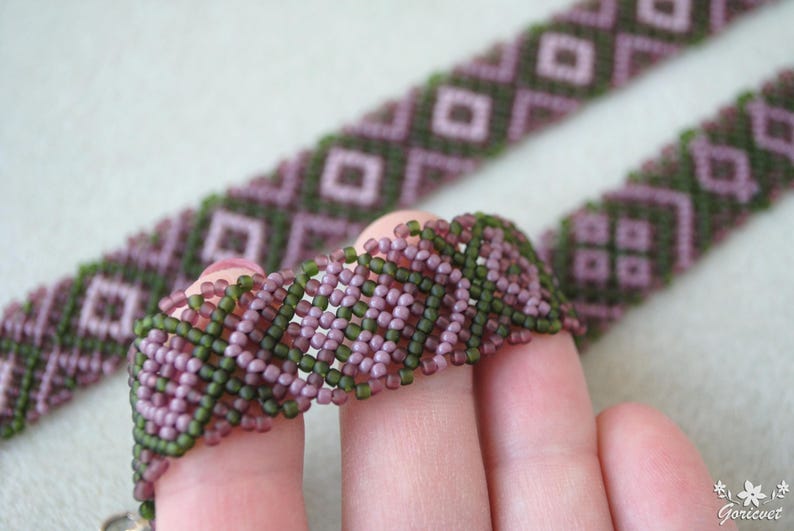 Pu&ograve; includere: Un primo piano di un braccialetto di perline con un motivo geometrico in tonalit&agrave; viola e verde.