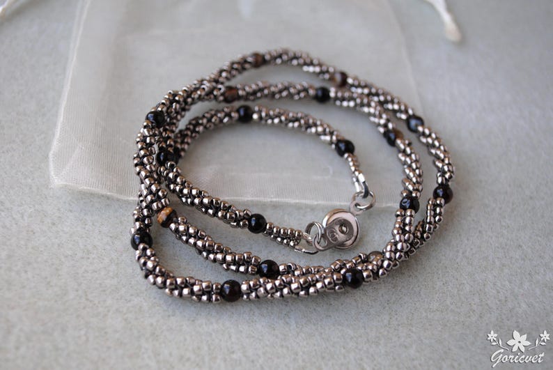 Op de afbeelding: Een zilveren en zwarte kralenketting met een magneetsluiting. De ketting is gemaakt van kleine, ronde kralen en heeft een gelaagd ontwerp.