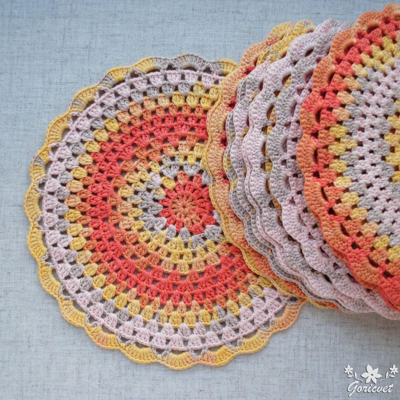 Puede incluir: Un conjunto de tapetes de ganchillo hechos a mano en tonos naranja, amarillo y gris. Los tapetes circulares tienen un borde festoneado y un dise&ntilde;o calado detallado. Los colores del hilo crean un efecto degradado.