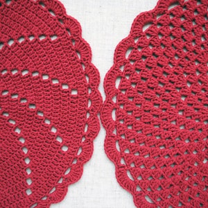 Pu&ograve; includere: Due tovagliette all'uncinetto rosse con un design circolare. Le tovagliette hanno un bordo a festoni e un motivo delicato.