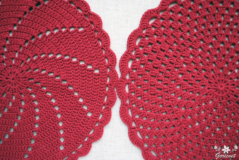 Pu&ograve; includere: Due tovagliette all'uncinetto rosse con un design circolare. Le tovagliette hanno un bordo a festoni e un motivo delicato.