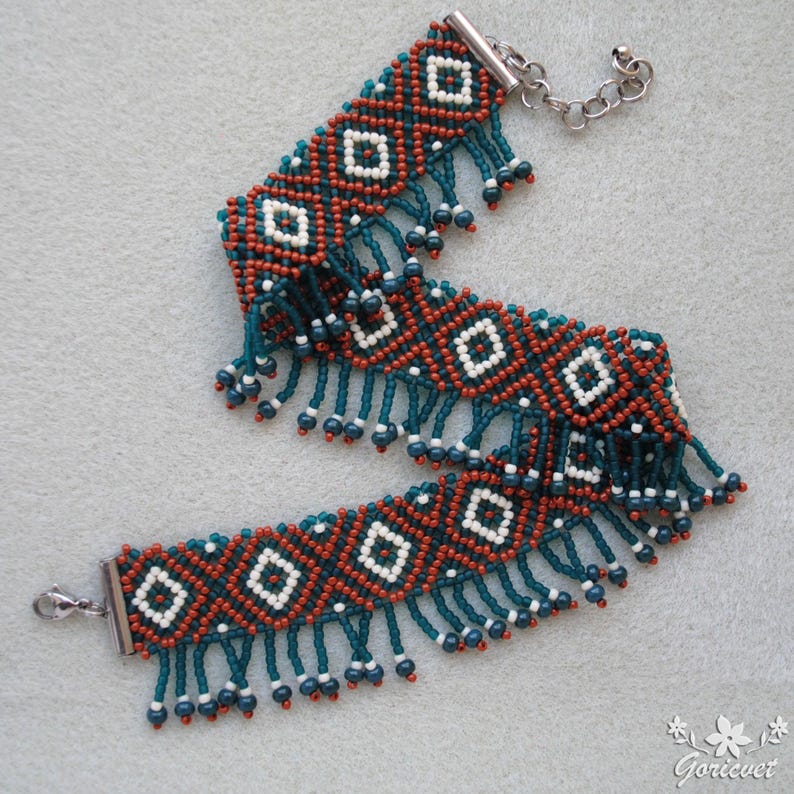 K&ouml;nnte beinhalten: Handgefertigtes Perlenarmband mit geometrischem Muster in Rost-, Wei&szlig;- und T&uuml;rkist&ouml;nen. Das Armband hat einen t&uuml;rkisfarbenen Fransenbesatz und einen silberfarbenen Verschluss. Ein einzigartiger Schmuck.