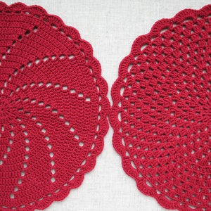 Pu&ograve; includere: Due tovagliette all'uncinetto rosse con un design circolare. Le tovagliette hanno un bordo a festoni e un centro con un motivo a spirale.