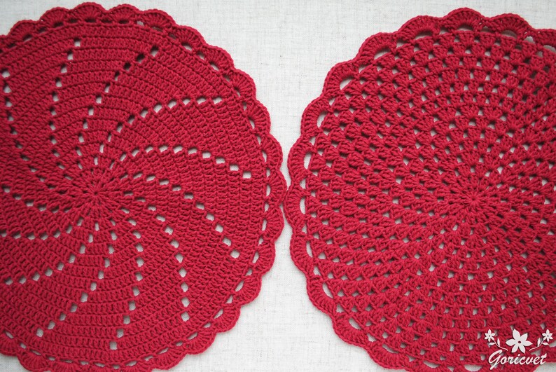 Pu&ograve; includere: Due tovagliette all'uncinetto rosse con un design circolare. Le tovagliette hanno un bordo a festoni e un centro con un motivo a spirale.