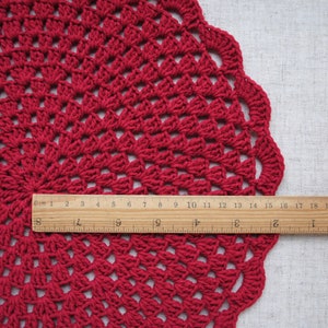 Pu&ograve; includere: Un tovaglietta all'uncinetto rossa con un bordo a festoni. La tovaglietta ha un diametro di circa 48 cm.