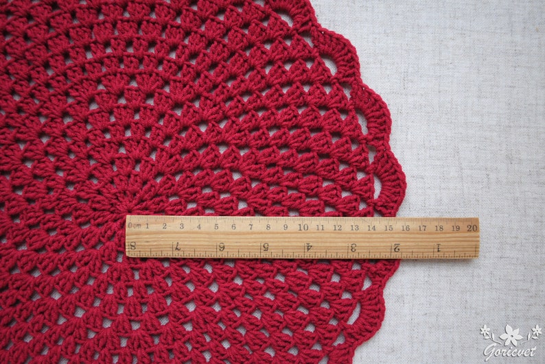 Pu&ograve; includere: Un tovaglietta all'uncinetto rossa con un bordo a festoni. La tovaglietta ha un diametro di circa 48 cm.