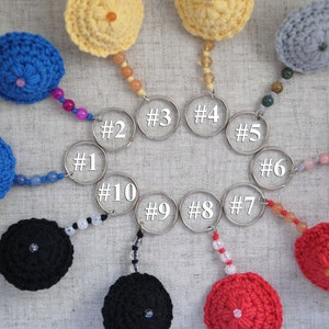 May include: Ten crocheted keyrings in various colours, including blue, red, yellow, black, and grey. Each keyring features a small crocheted ball with a beaded chain and a silver key ring.