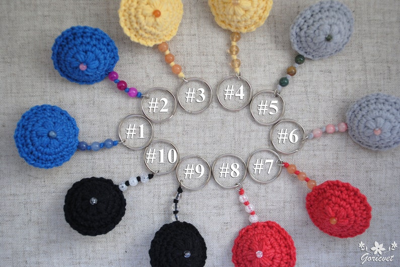 May include: Ten crocheted keyrings in various colours, including blue, red, yellow, black, and grey. Each keyring features a small crocheted ball with a beaded chain and a silver key ring.