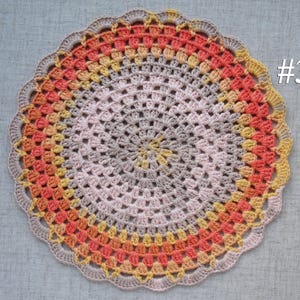 Puede incluir: Un tapete de ganchillo circular hecho a mano en tonos melocot&oacute;n, amarillo y gris. El tapete presenta un borde festoneado y un dise&ntilde;o central en espiral. El n&uacute;mero "#3" es visible en la esquina superior derecha.