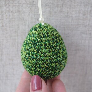 Pu&ograve; includere: Un ornamento a forma di uovo in crochet verde e bianco con un perlino bianco in cima.