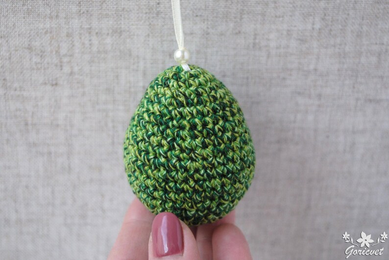 Pu&ograve; includere: Un ornamento a forma di uovo in crochet verde e bianco con un perlino bianco in cima.