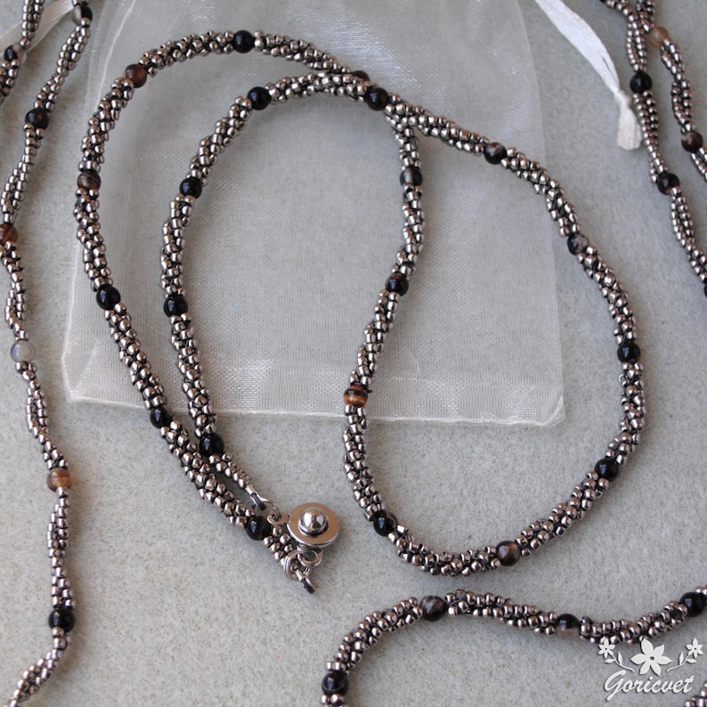 Op de afbeelding: Een zilveren en zwarte kralenketting met een magneetsluiting. De ketting is gemaakt met kleine, ronde kralen en heeft verschillende kleuren, waaronder zilver, zwart en bruin.