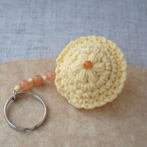 May include: A yellow crocheted keychain with a small orange bead in the centre. The keychain has a silver key ring and a chain of orange beads.