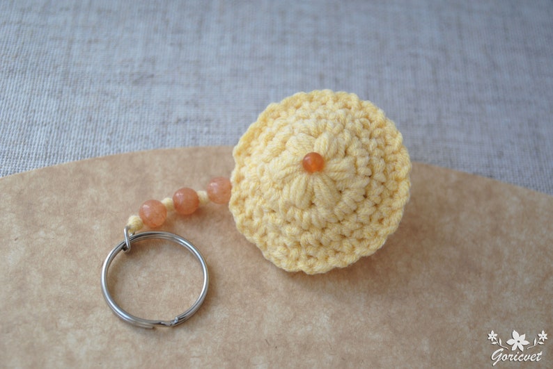 May include: A yellow crocheted keychain with a small orange bead in the centre. The keychain has a silver key ring and a chain of orange beads.