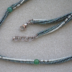 May include: A delicate necklace made with small, graduated blue and white beads, accented with two green gemstone beads. The necklace has a silver clasp and chain.