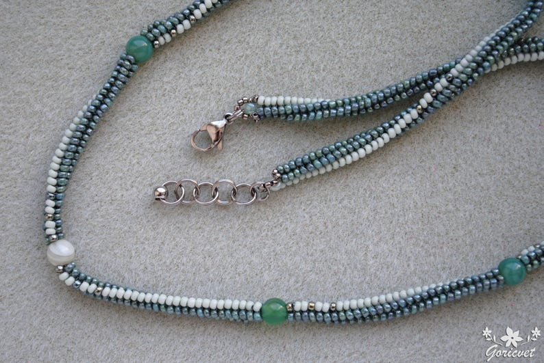 May include: A delicate necklace made with small, graduated blue and white beads, accented with two green gemstone beads. The necklace has a silver clasp and chain.