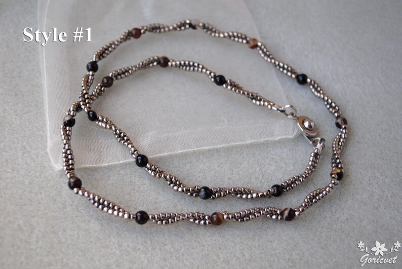 Op de afbeelding: Een zilveren ketting met zwarte en bruine kralen. De ketting is dubbelstrengs en heeft een sluiting. De tekst "Style #1" is zichtbaar in de afbeelding.