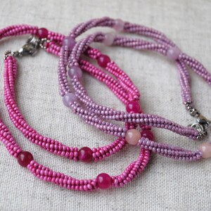 Puede incluir: Dos collares de cuentas, uno rosa y otro morado, con cuentas de piedras preciosas m&aacute;s grandes intercaladas.